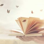Otwarta książka w dłoni, wokół której latają motyle.