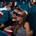 Para oglądająca film w kinie w okularach 3D, trzymając napoje i popcorn.