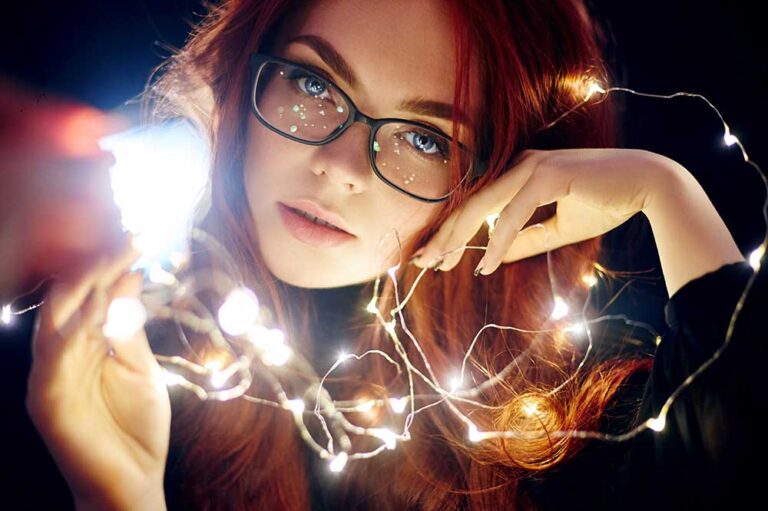 Kobieta w okularach trzymająca światełka na ciemnym tle.