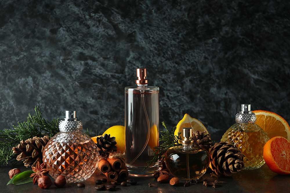 Butelki perfum otoczone cytrusami, szyszkami i przyprawami na ciemnym tle.