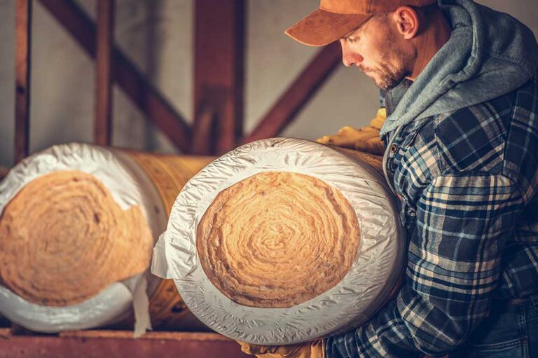 Mężczyzna w czapce trzyma duży zwój wełny mineralnej w magazynie.