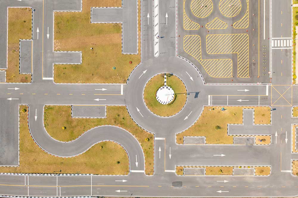 Obraz przedstawiający tor szkoleniowy dla kierowców widziany z lotu ptaka, zawierający rondo, pasy ruchu i oznaczenia poziome na drodze.