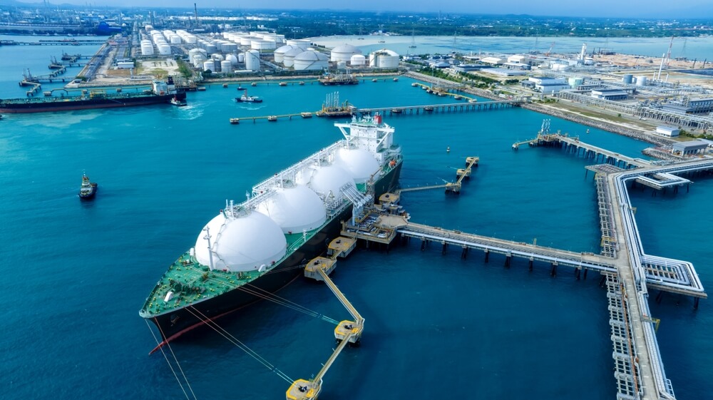 Tankowiec LNG przy nabrzeżu w porcie, w tle zakłady przemysłowe i zbiorniki magazynowe.