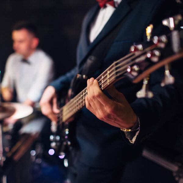 Muzyk grający na gitarze basowej, w tle perkusista.