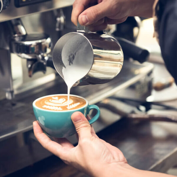 Barista nalewający spienione mleko do filiżanki kawy, tworząc wzór latte art.