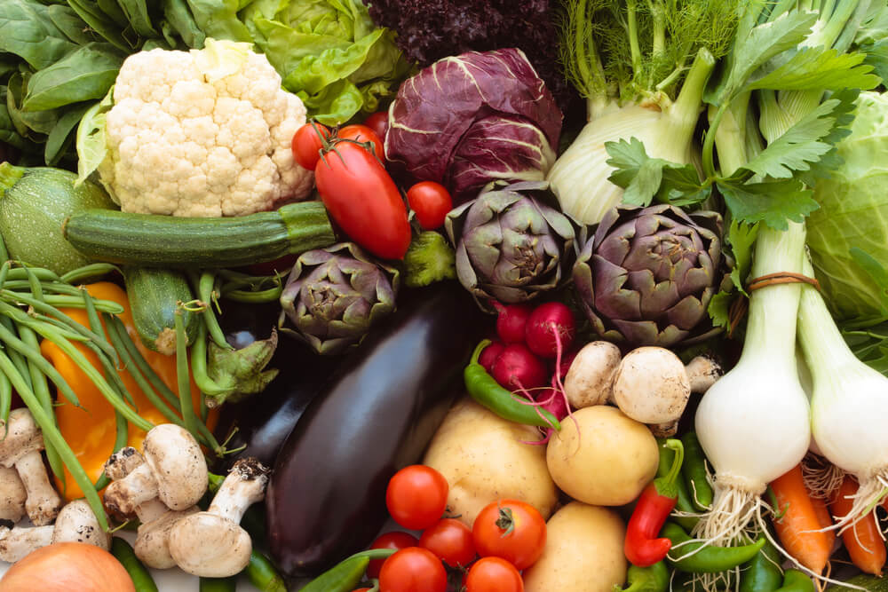 Różne rodzaje świeżych warzyw, w tym kalafior, bakłażan, karczochy, pomidory, papryka, grzyby, cebula, sałata i rzodkiewki.