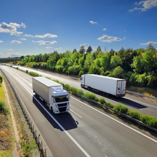 Ciężarówki jadące autostradą w otoczeniu zieleni pod błękitnym niebem z chmurami.