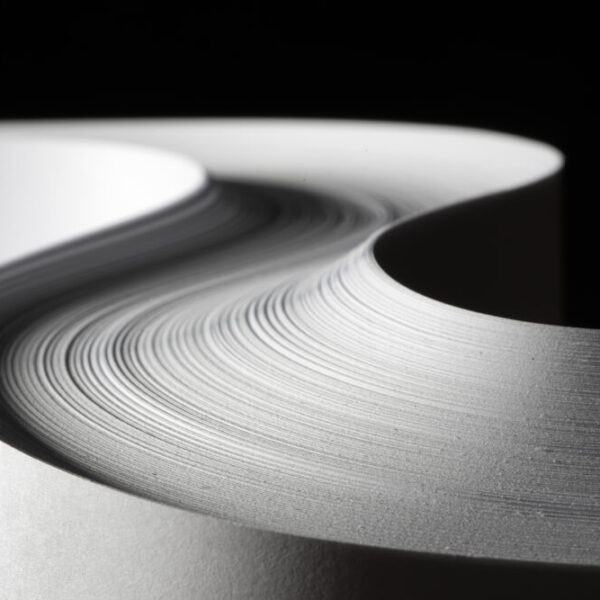 Zbliżenie na brzegi stosu papieru ułożonego w zakrzywioną formę, tworzące falisty wzór na tle czerni.