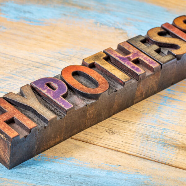 Drewniane litery tworzące słowo "HYPOTHESIS" na tle drewnianej powierzchni pomalowanej na niebiesko i brązowo.
