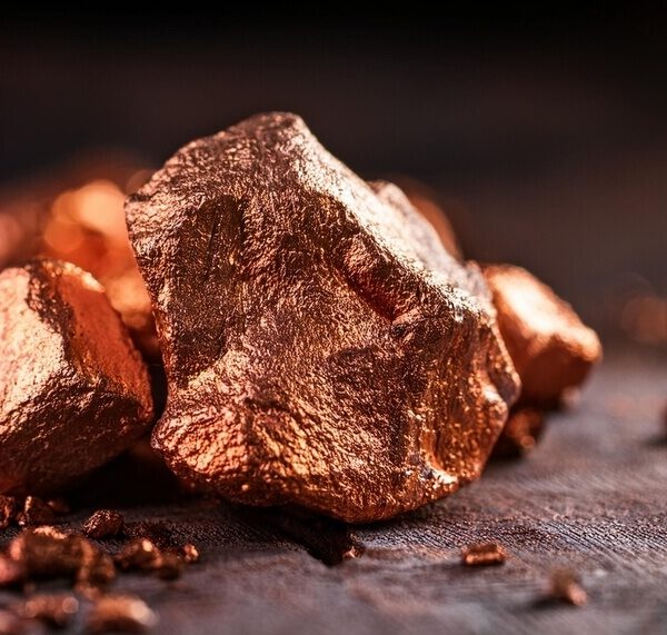 Bryła miedzi leżąca na ciemnym tle, z widoczną fakturą i połyskiem metalu.