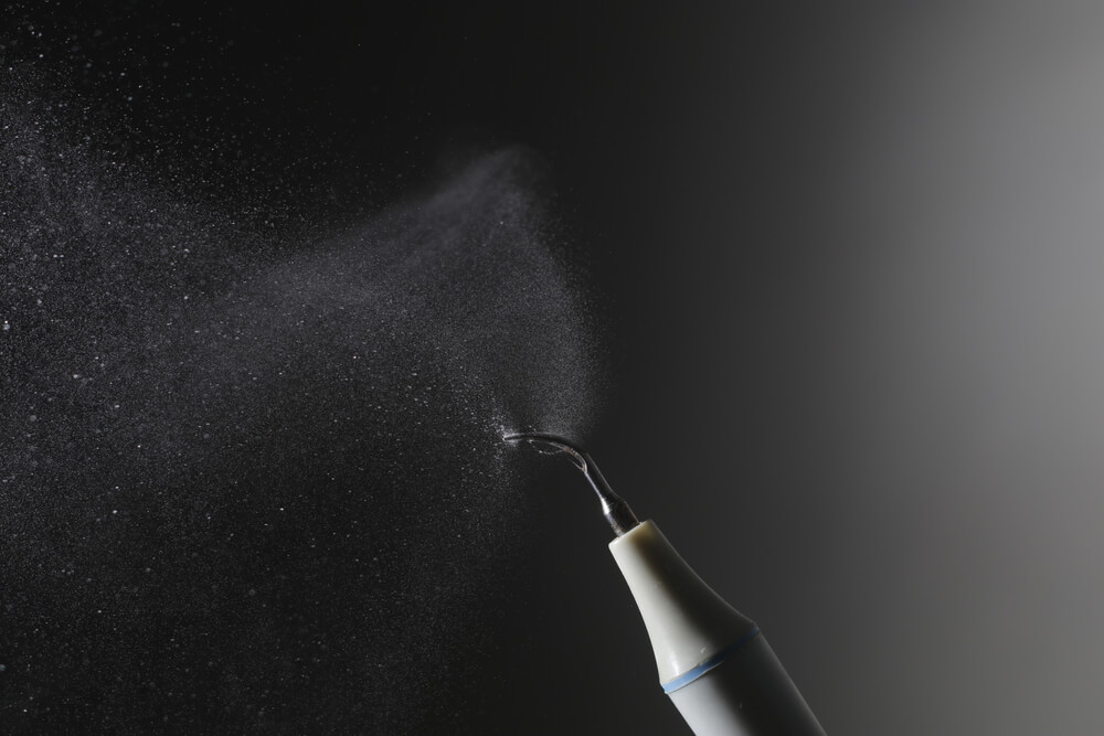 Strumień wody rozpylany z końcówki dentystycznego irygatora na ciemnym tle.